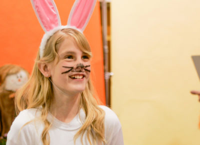 A elementary girl dress up as a bunny with rabbit ears on her head.