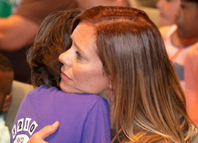 A woman volunteer hugs a child. Her eyes look very empathetic.