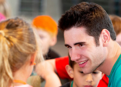 A college-aged volunteer sits and smiles at his small group of students.