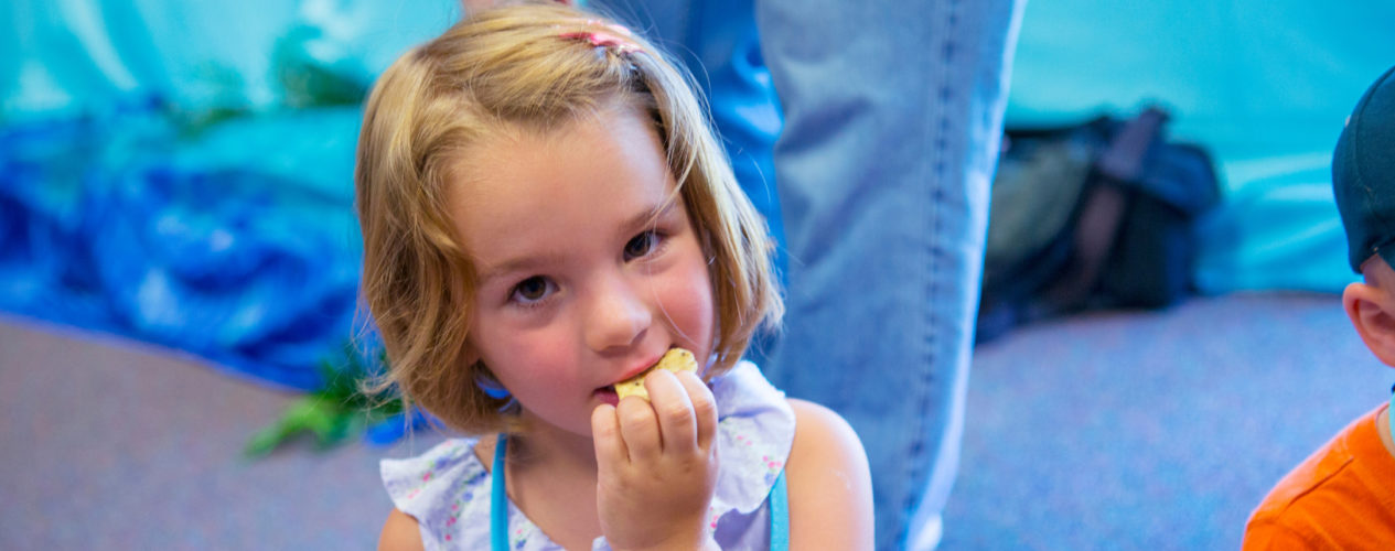 An elementary-aged girl is eating a snack she made from a recipe.