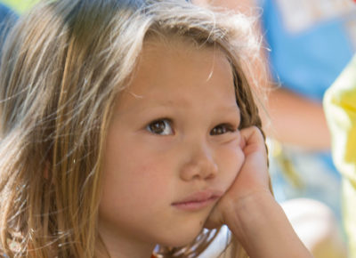 An elementary aged girl is resting her cheek on her hand. She looks very bored.