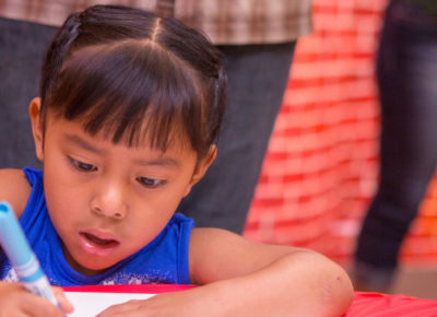 A preschool girl is coloring with her mouth wide open as she participates in the Bible craft.
