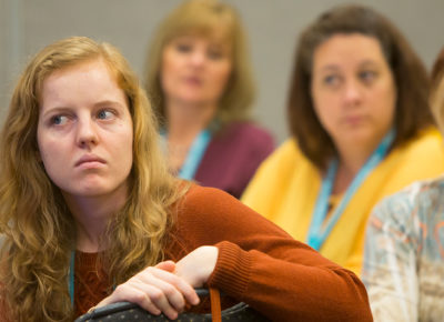 A woman volunteer who is a narcissist stars grumpily at the person talking.