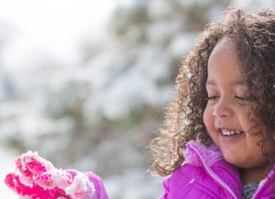 An early elementary aged girl smiles as she plays outside in the snow.