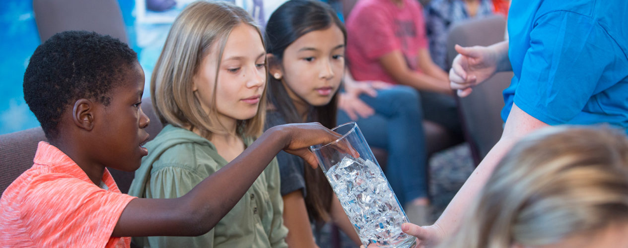 A group of three preteens group some ice cubes out of a jar.