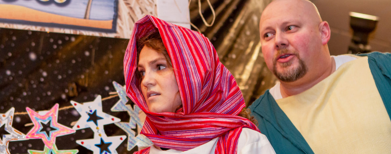 A woman volunteer in Biblical clothing with a pink head scarf acts of a Bible scene with a man also dressed in Biblical clothing.
