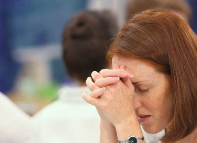 A woman with her hands folded to her head in prayer.