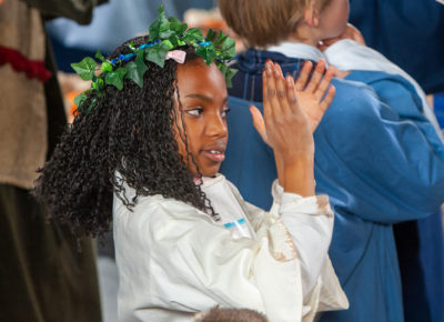 An older elementary girl dressed in Roman attire claps her hands.