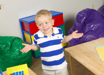 A preschool aged boy shrugs with toys all around him.