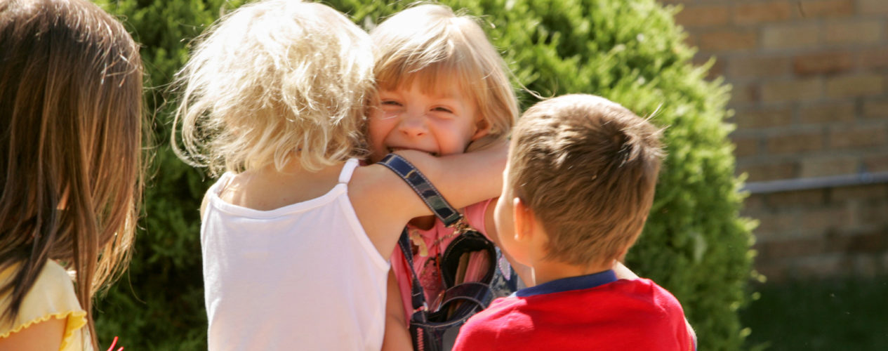 A group of three children are hugging as they joyfully play outside.