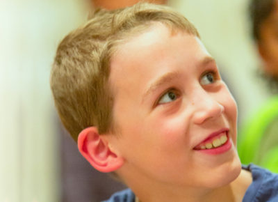 A preteen boy smiles up and over his shoulder.