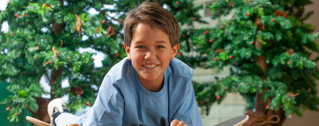 A preteen boy smiling as he lays in front of a Christmas tree using his homemade gift wrap to wrap gifts.
