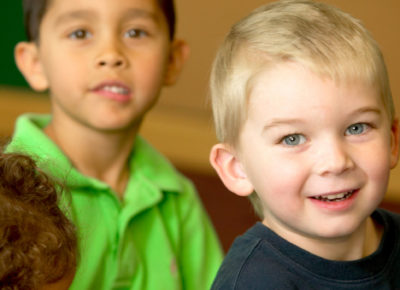 Two kindergarten boys sit on a carpet smiling.