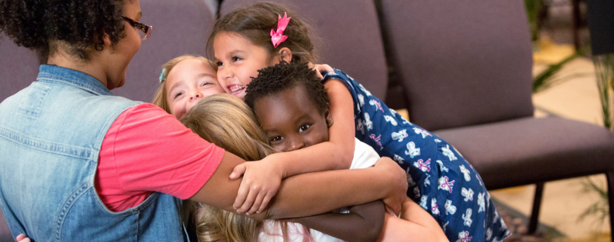 A group of four elementary children hugging their small group leader.