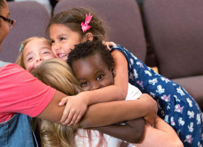 A group of four elementary children hugging their small group leader.