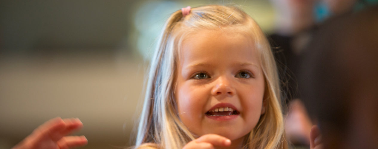 A preschool-aged girl smiles and points her finger.