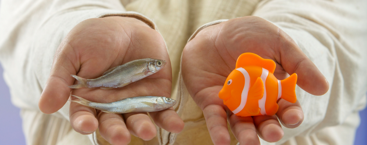 A man in Biblical clothes holding to minnows in one hand and a plastic goldfish in the other.