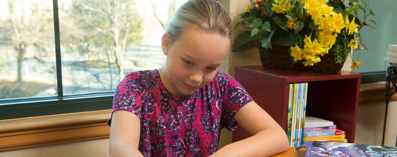 A preteen girl sits at a craft table.
