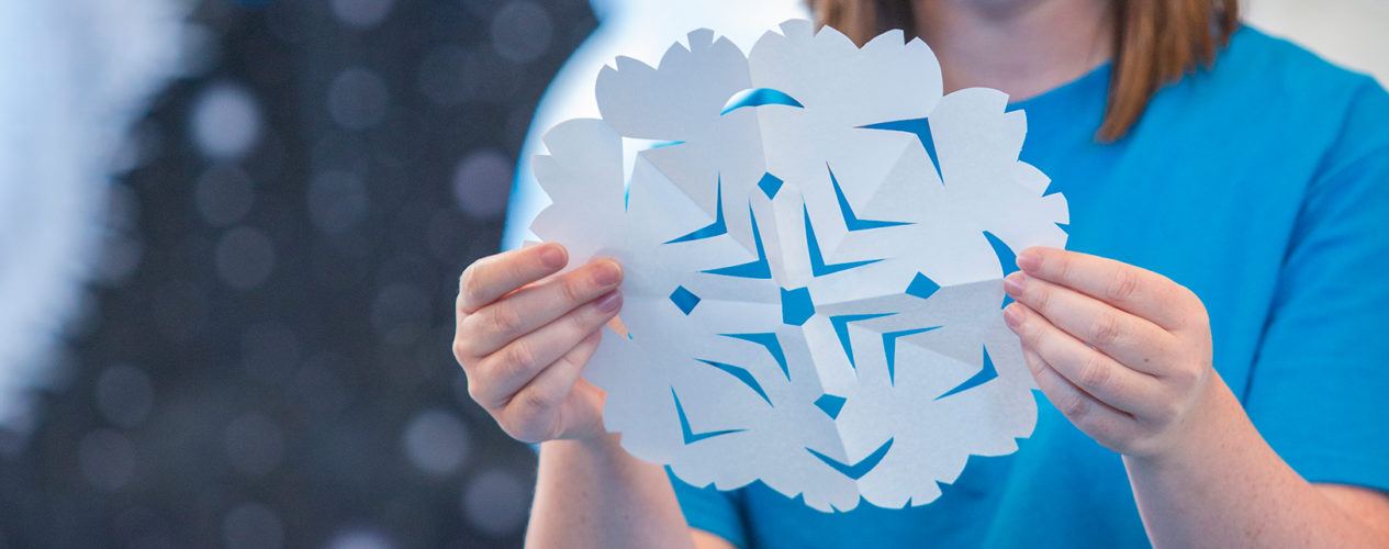 A room leader creates a snowflake cut out of paper for a marvelous season winter bulletin board.