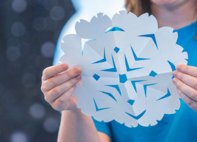 A room leader creates a snowflake cut out of paper for a marvelous season winter bulletin board.