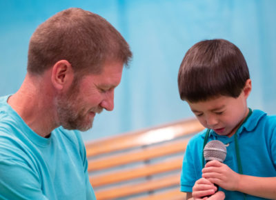 A male volunteer is praying with an early elementary boy during one of the faith milestones.