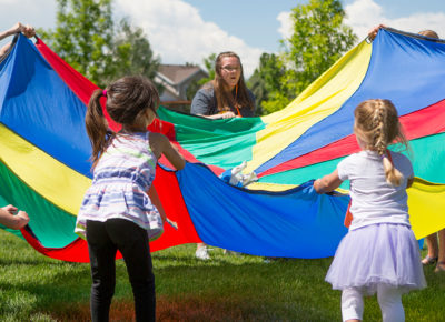 A group of children play outside with a parachute at an affordable program.