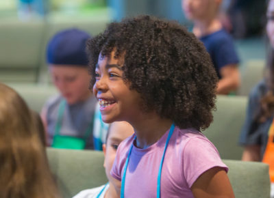 An elementary girl smiles excitedly as she participates in a lesson.