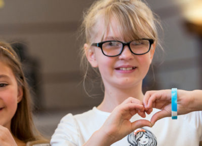 Two older elementary girls make heart-hands as they smile at the camera.