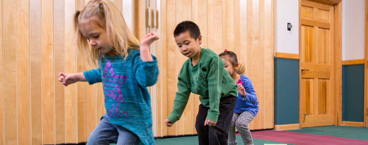 Three first-graders hop from one side of the room to another.