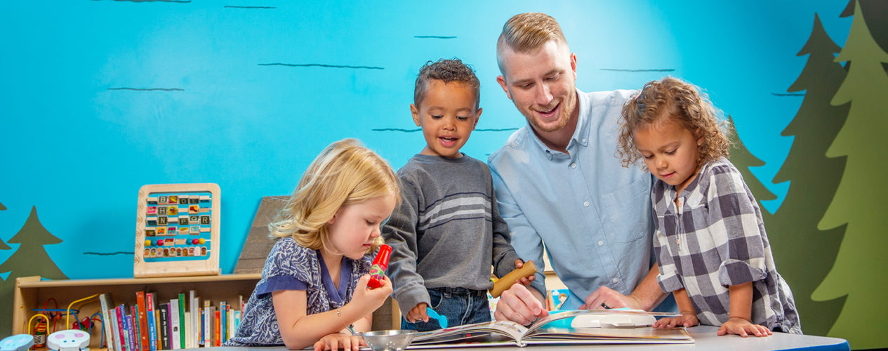 A male volunteer works with three preschoolers in a fun children's ministry room.