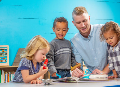 A male volunteer works with three preschoolers in a fun children's ministry room.