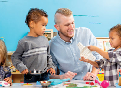 A male volunteer sitting at a table with four preschoolers. They are doing a craft.