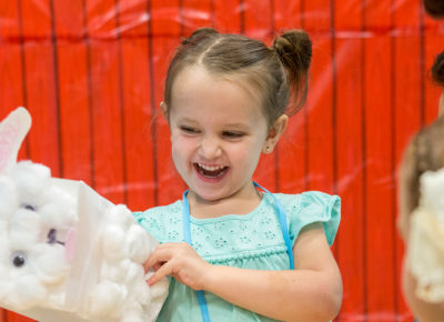 A preschool girl smiling excitedly as she plays with a puppet.