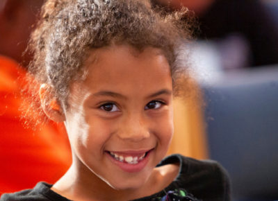Preteen girl smiles at the camera. She is sitting in her classroom area.