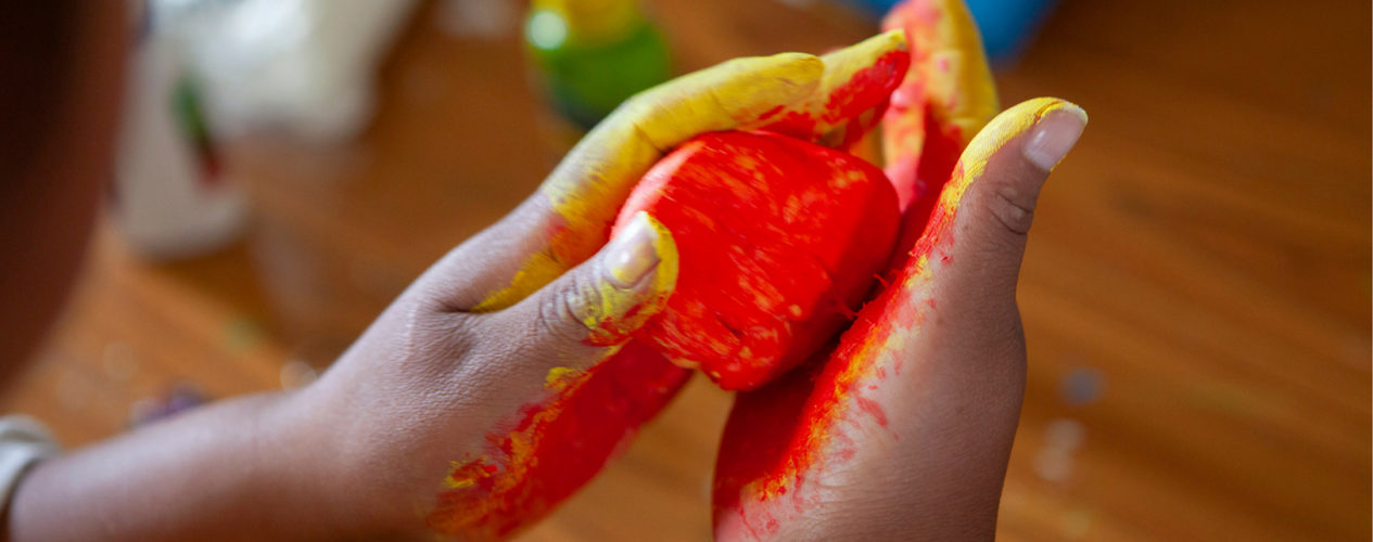 A pair of hands are shaping clay with yellow and red paint on it.