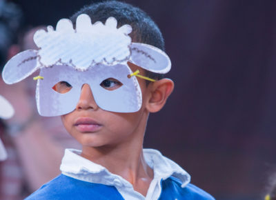 An elementary-aged boy is wearing a sheep mask as he looks around.