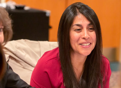 A woman smiling as she sits at a table talking to other adults.