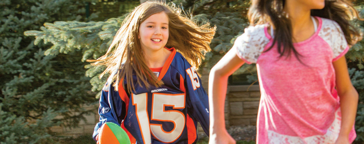 Two preteen girls are playing football. One girl is wearing a jersey and carrying a football.
