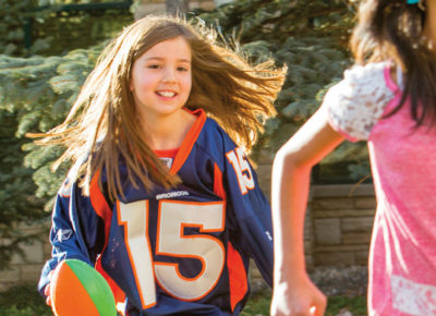 Two preteen girls are playing football. One girl is wearing a jersey and carrying a football.