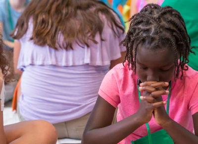 A preteen girl bows her head in prayer.