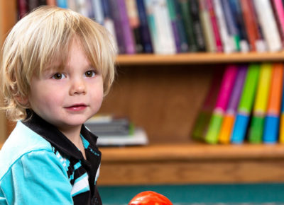 Preschool boy sitting on the ground of his classroom holding a toy in his lap.