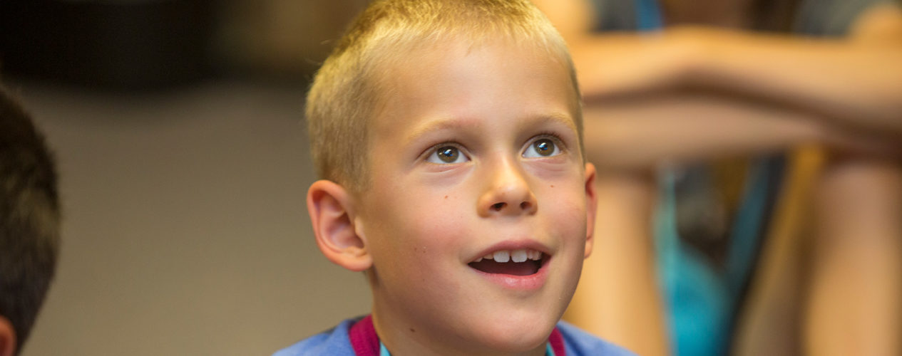 An elementary boy smiles in awe while learning about the miracles of Jesus.