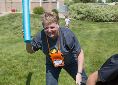 A female volunteer with a water noodle in her hand chases a preteen.