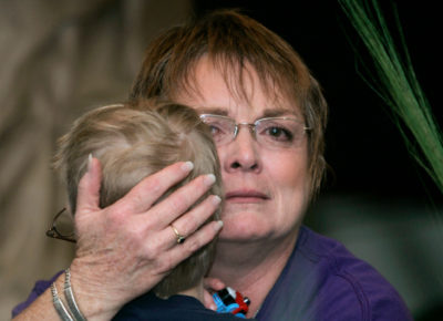 A woman, who looks very sad, pulls a young boy in for a hug. She has her hand on the back of his head. She seems to be apt at helping children grieve in a healthy way.