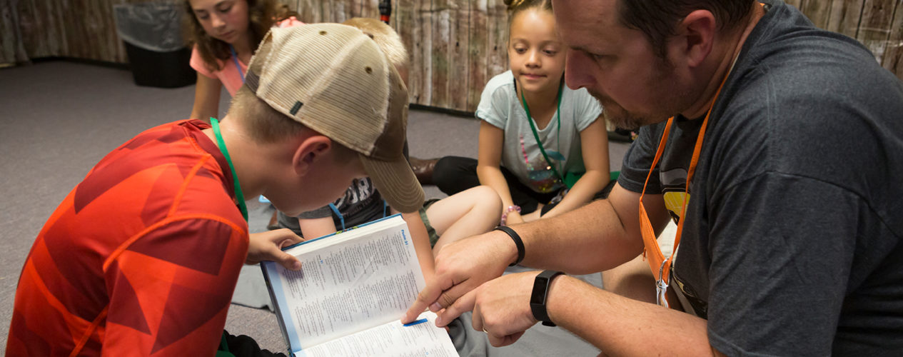 A male leader helps a boy look up a verse as a way to increase his Biblical truth.