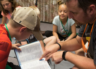 A male leader helps a boy look up a verse as a way to increase his Biblical truth.