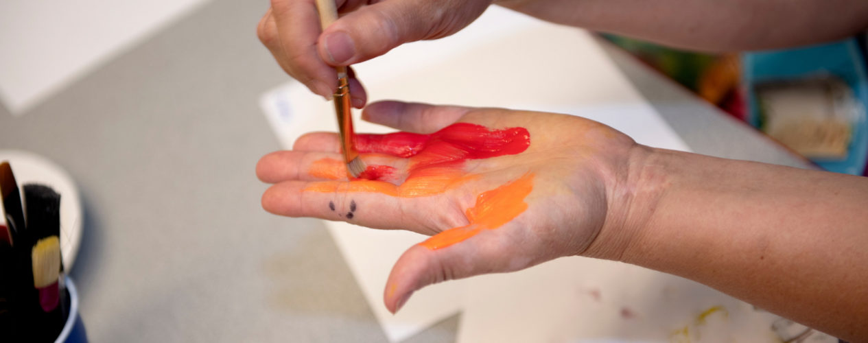 One small hand is applying red and orange paint to another small hand.