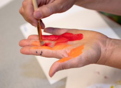 One small hand is applying red and orange paint to another small hand.