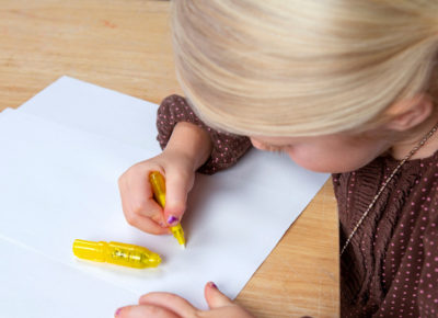 Elementary-aged girl writing on a white sheet of paper.