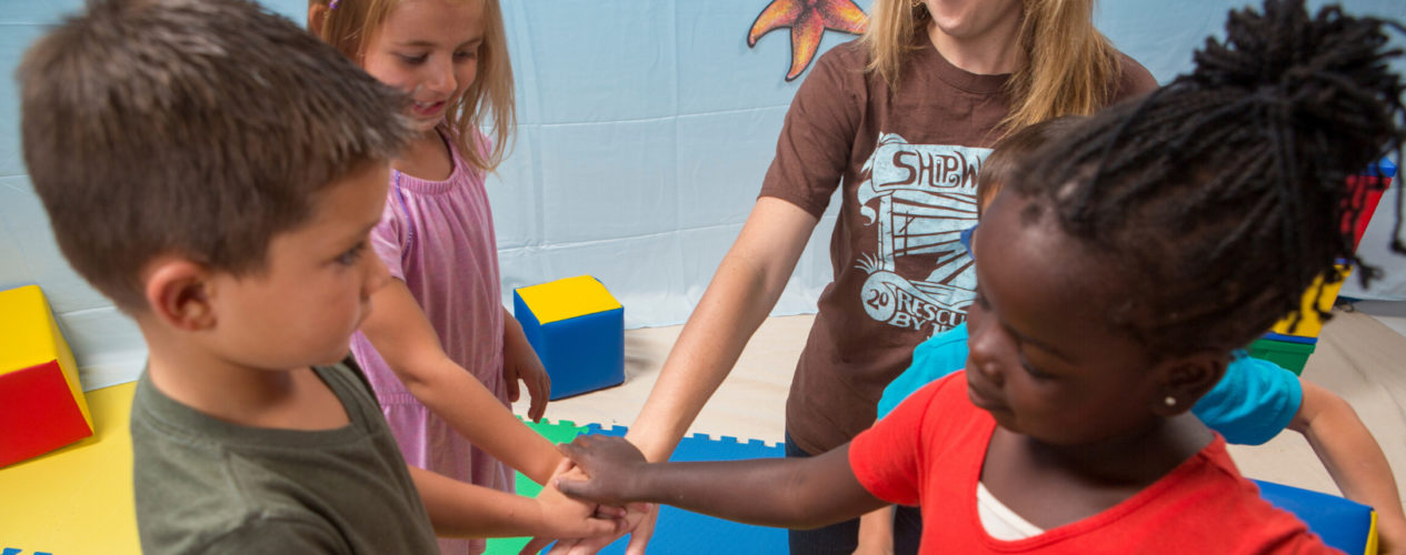 A volunteer and three preschoolers put their hands together for a cheer in their newly utilized space.